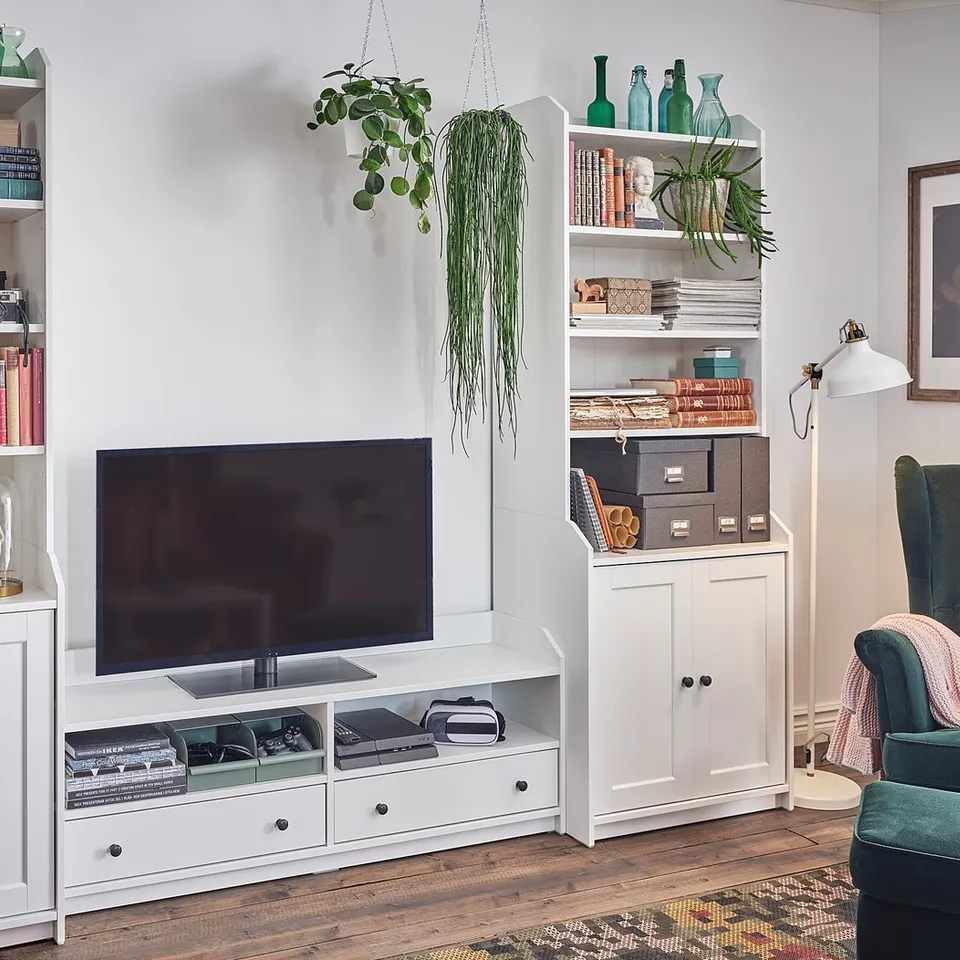 Modern living room with white HAUGA tv unit, featuring shelves with books, vases, and decor. Includes a flat-screen tv and green accent chair.