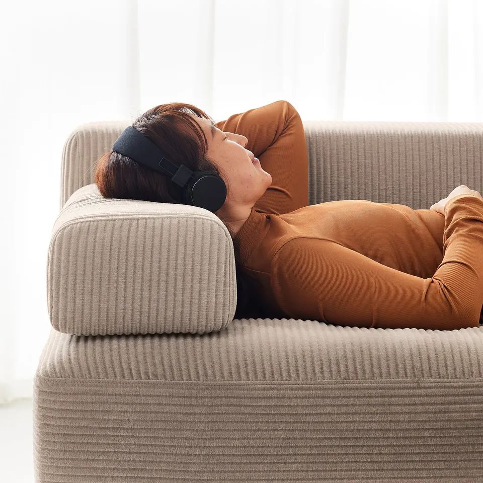 A person relaxes on a beige JÄTTEBO modular sofa, listening to headphones. The sofa is stylish with clean lines.