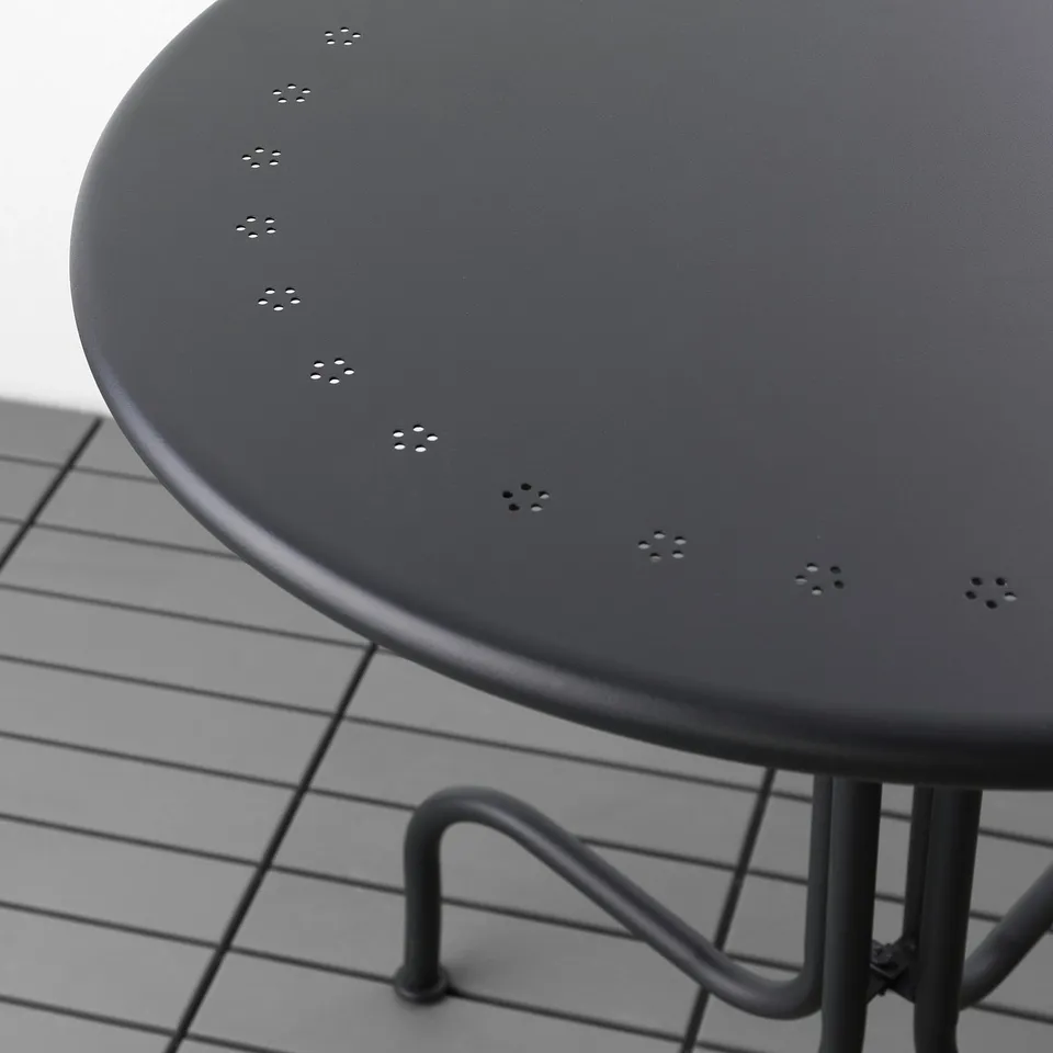 Black round outdoor table with intricate cutouts for water drainage, supported by sturdy metal legs.