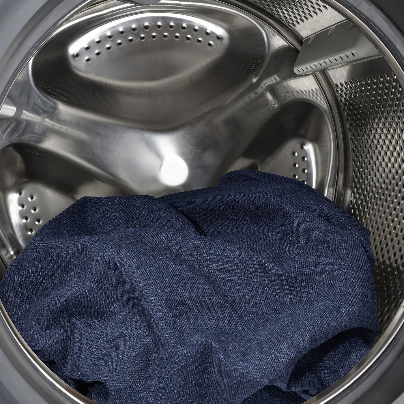 Washing machines stainless steel drum with dark jeans inside, ready for cleaning.