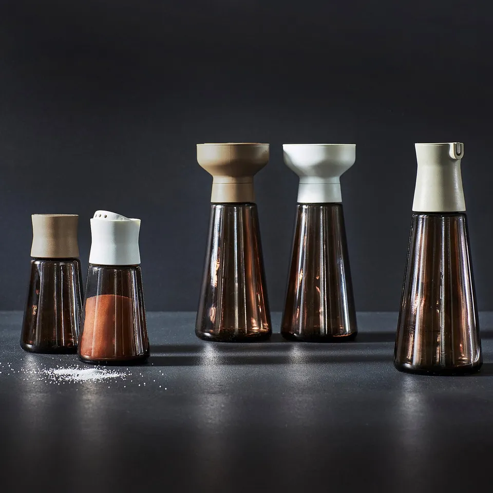 Four brown glass HALVTOM jars with wooden and white lids, containing salt and spices, arranged for kitchen and dining use.