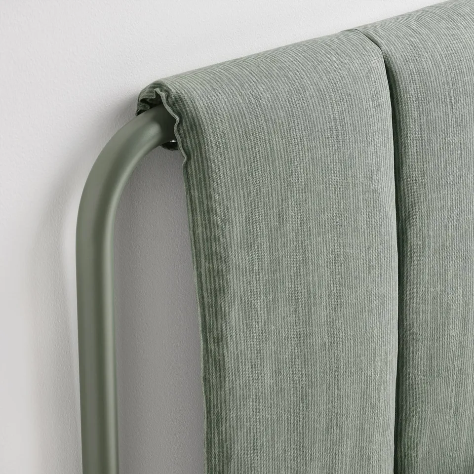 A close-up of a grey-green upholstered headboard corner, showing high-quality fabric and metal frame construction.