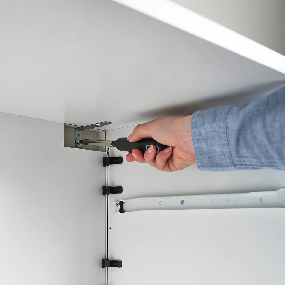 Person using screwdriver to assemble LASTARE cabinet. The installation process of the simple, versatile storage system.