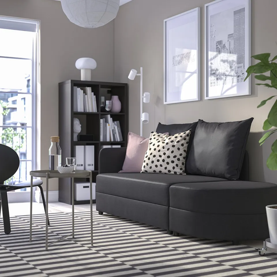 Modern living room with LINDÅKRA sofa bed, black/white decor, bookshelf, & large window.