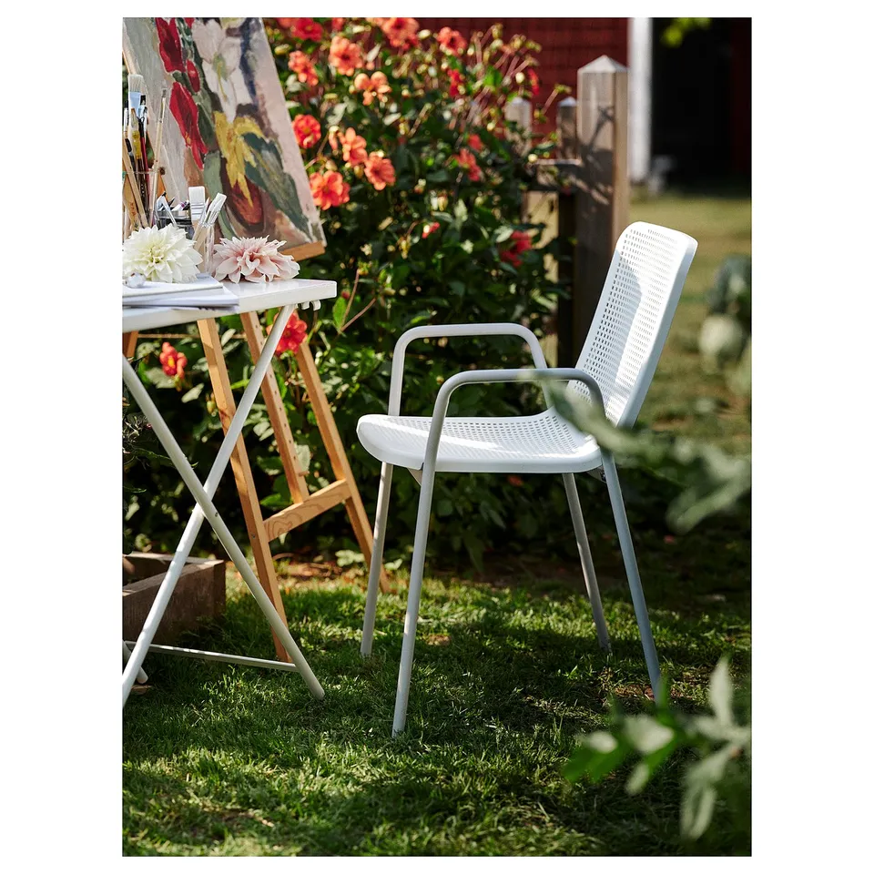 White outdoor chair in garden, made of plastic and metal, with back and arm supports, near table.