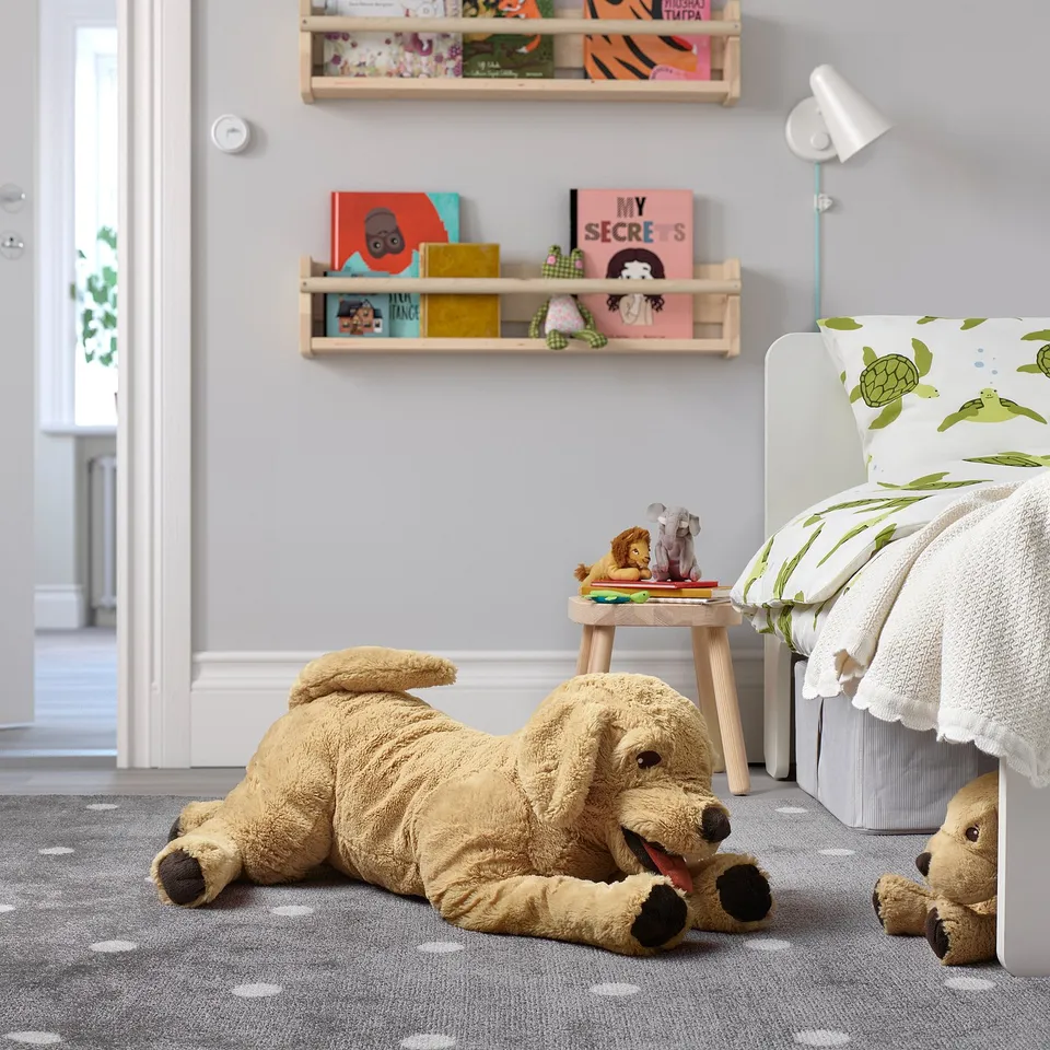 Large plush golden retriever toy in kids cosy bedroom. Bright, soft, and relaxes beside a bed with turtle pillows. Books and smaller toys nearby.