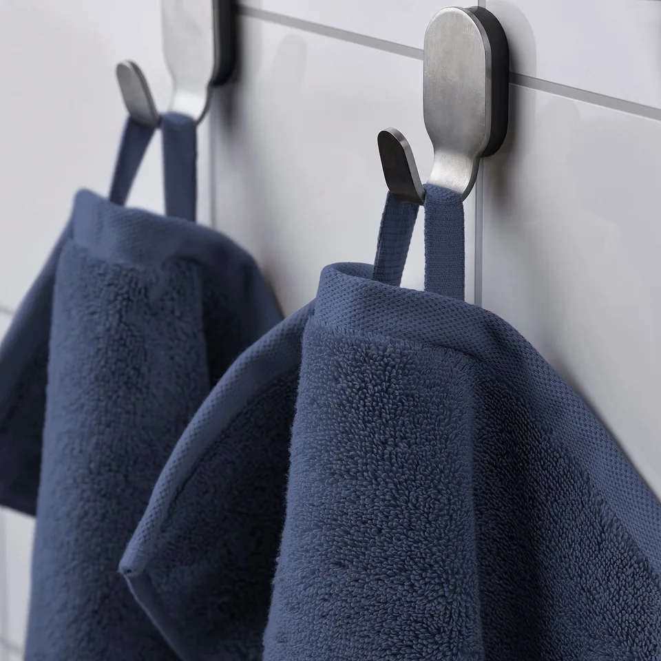 Two navy blue towels hang on metal hooks against white tiles.