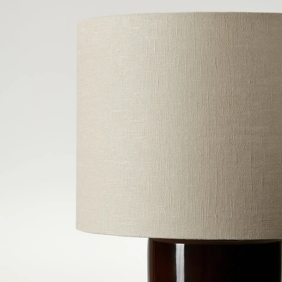 Cylindrical beige linen lamp shade on dark base, reflecting quality craftsmanship.