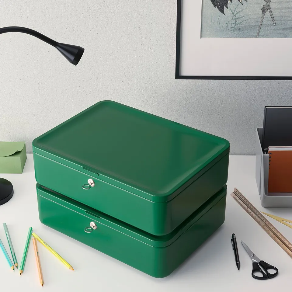 Green double-stack metal storage boxes on desk with stationery, near lamp and picture frame.