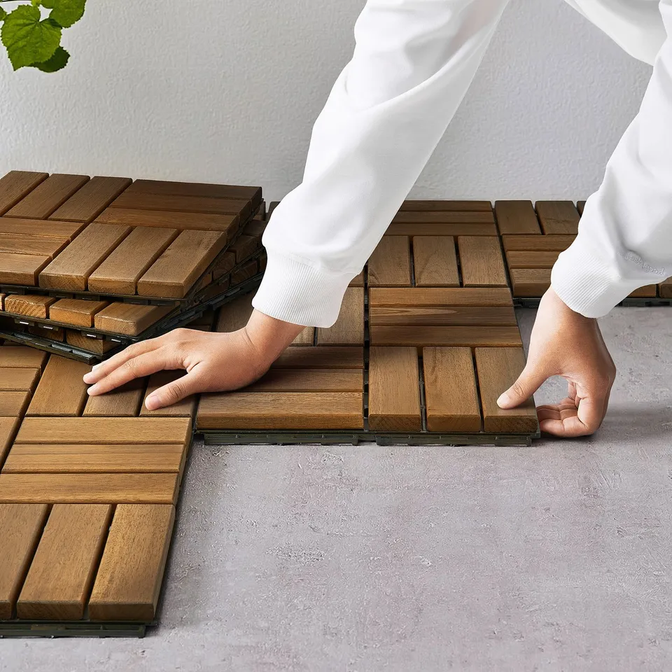 Person assembling wooden RUNNEN deck tiles, creating a terrace or balcony floor.