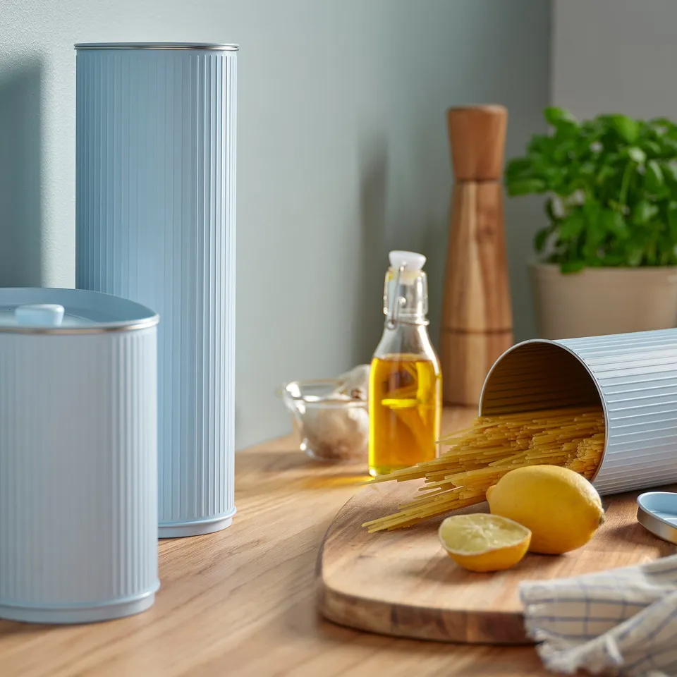 Kitchen scene with blue BETTHAJ tins, lemon, olive oil, herbs, pastas on table.