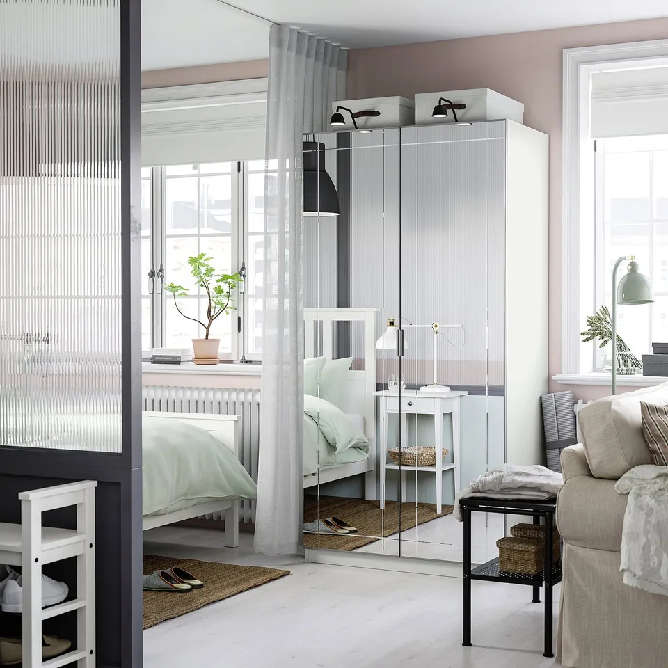 Modern bedroom with KAMMARTORP mirrored wardrobe, bed, side table, lamp, and armchair.