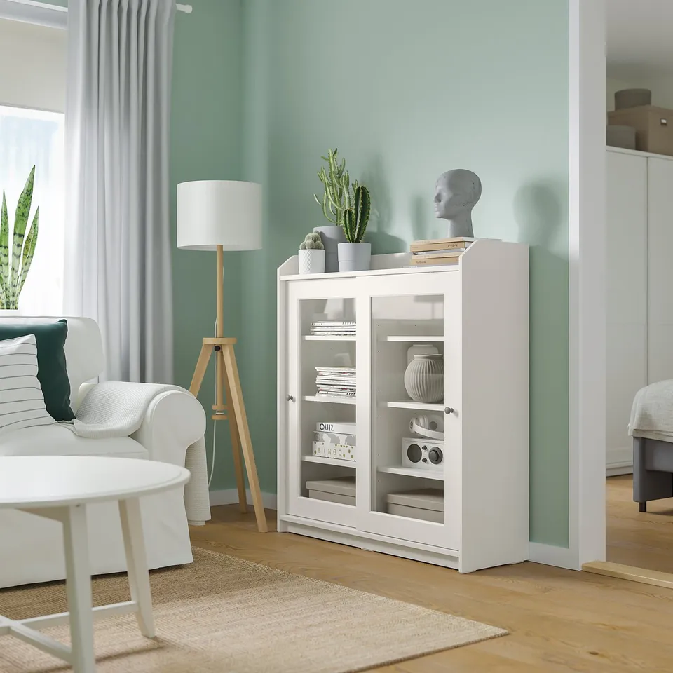 Living room with white HAUGA cabinet, lamp, and sofa. Green wall, wooden floor.