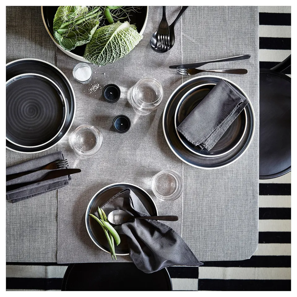 SVARTSENAP grey cotton tablecloth with placemats, dark plates, glassware, and black cutlery. Modern minimalist dining setup.