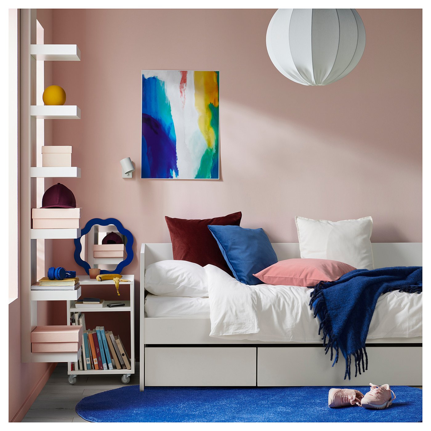A modern bedroom a white VIHALS daybed with colourful pillows, a vibrant rug, and a blue abstract wall art.