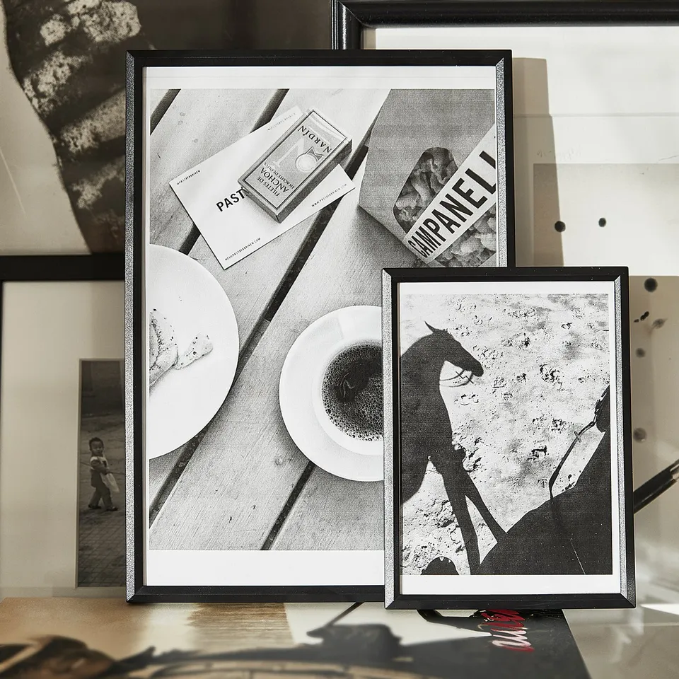 Black framed pictures lean against wall; one shows plate, another horse silhouette; artistic shadow play.