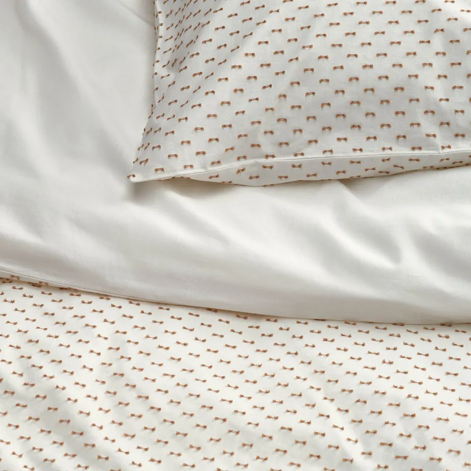 Close-up of white bedding with subtle orange woven pattern, showcasing soft texture and quality cotton material.