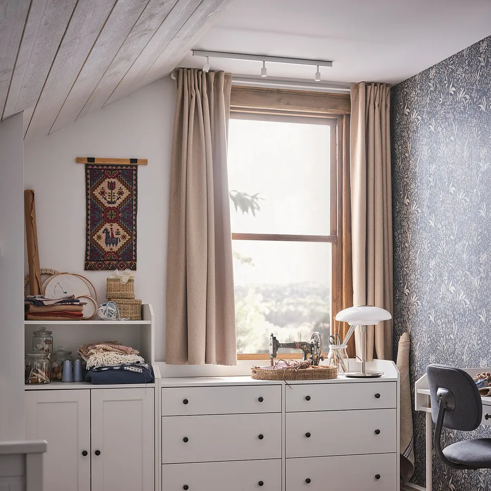 Cosy home office with white HAUGA chest and shelves, beige curtains, and a patterned rug on wooden floor.