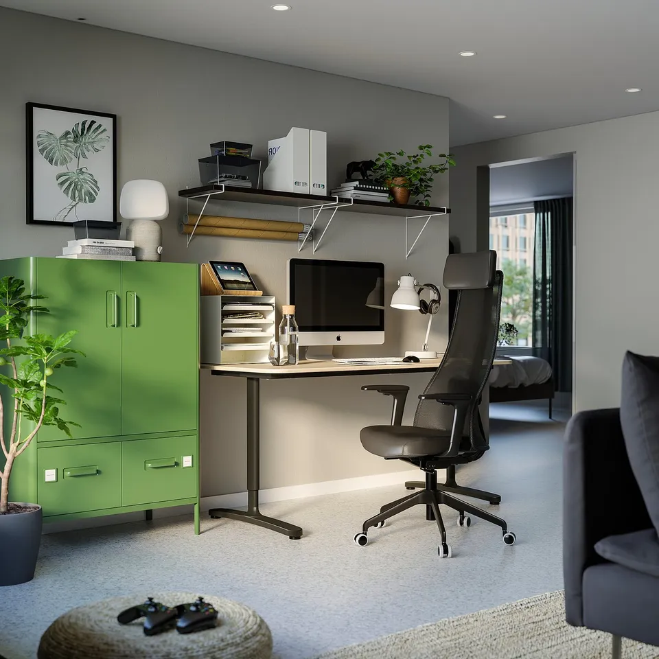 Modern home office with green cabinet, black ergonomic office chair, wooden desk, computer, shelves with books, and grey couch.