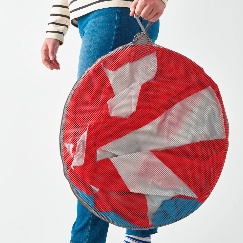 A person holding a red and white mesh tent in a bag, for childrens play or hiding.