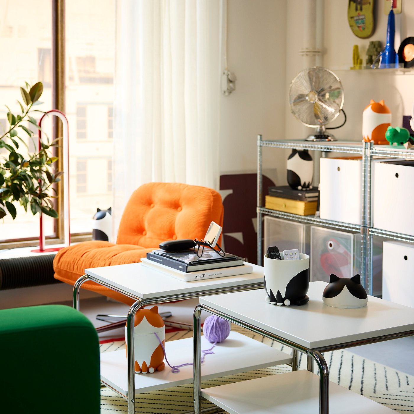 Bright living room with white furniture, cat organisers, orange chair, green stool, and decorated shelves.
