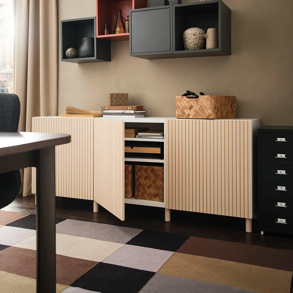 Modern room with beige walls, a light wooden cabinet, several shelves, decorative items, and a multicoloured geometric rug.