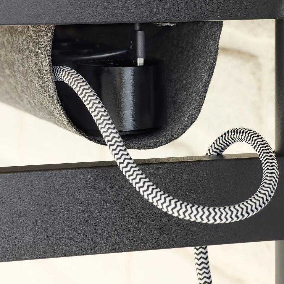 Black zigzag-patterned power cord under black desk, showing charging station.