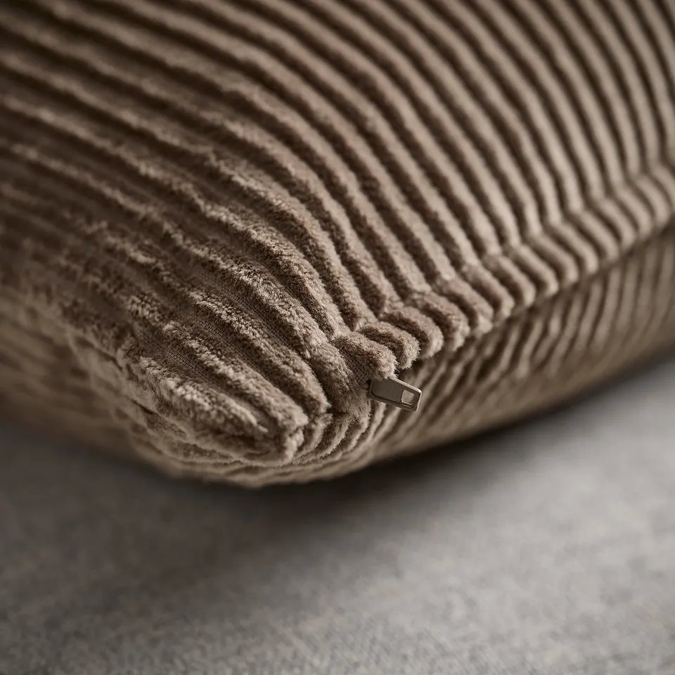Close-up of plush, striped cushion cover in soft gray-brown corduroy, showcasing its textured fabric and hidden zip closure.