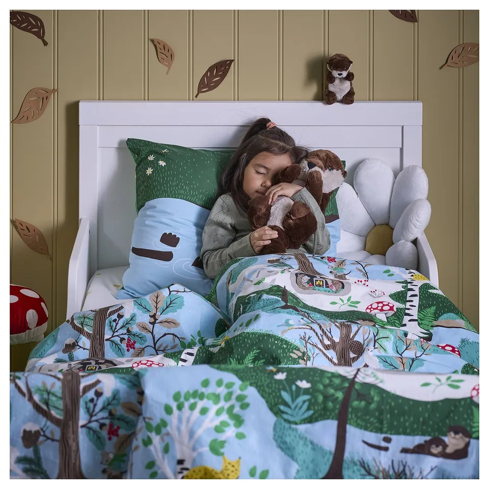 Child sleeping on bed with SKOGSDUVA collection: comfy forest-themed bedding and otter toys.