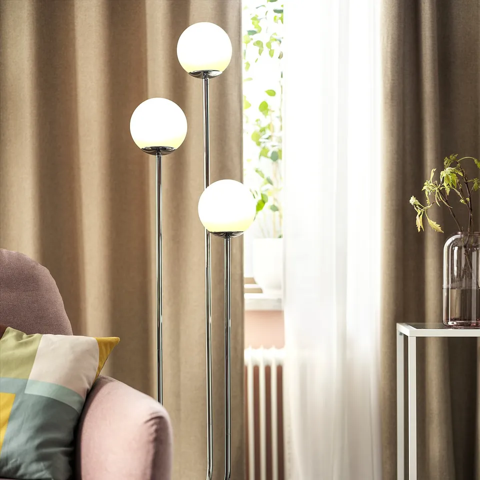A modern living room with a pink sofa, a multi-globe chrome lamp, curtains, and a side table with a vase.