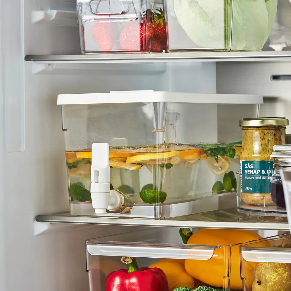 Open fridge with KLIPPKAKTUS container filled with water, fruit slices, and ice cubes, ready to dispense chilled beverage.