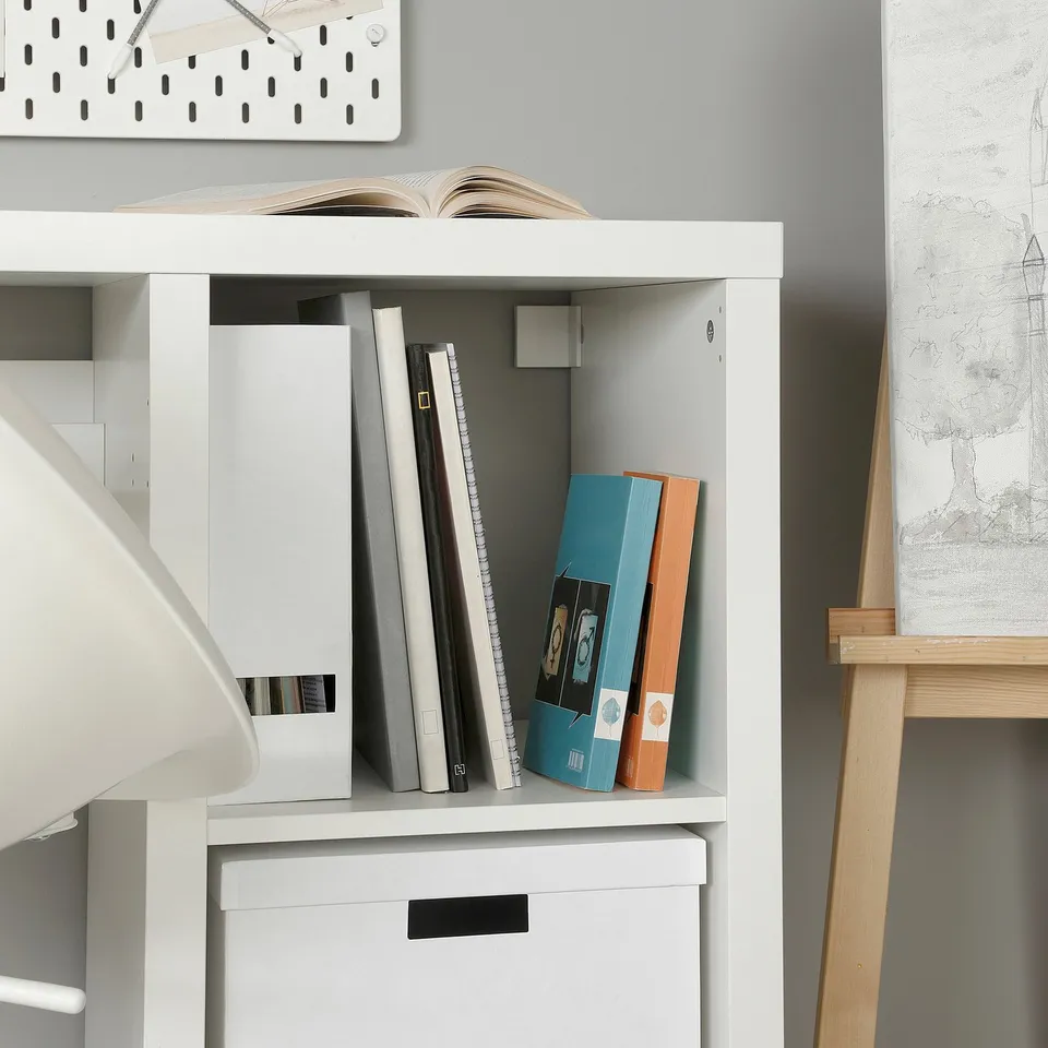 White KALLAX desk with storage boxes and books neatly organised. Grey wall art hangs above.