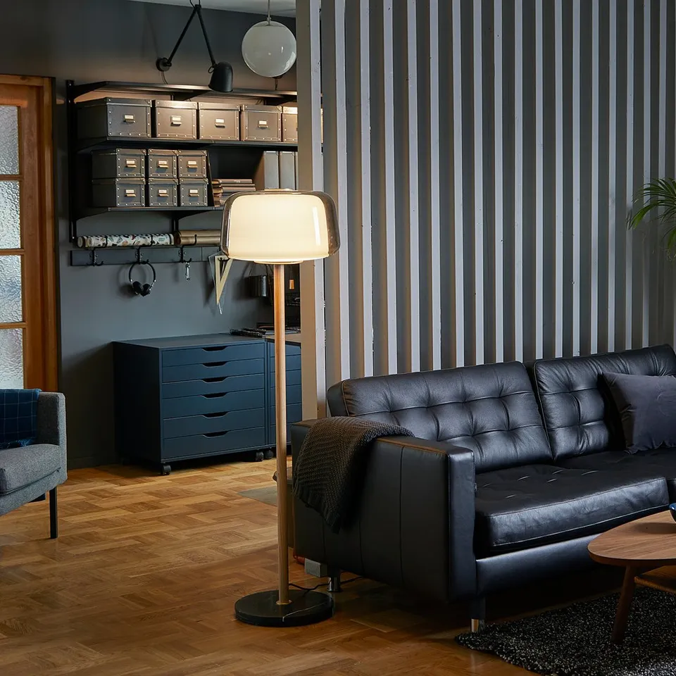 Modern living room with black leather LANDSKRONA sofa, wooden coffee table, floor lamp, and industrial decor elements.