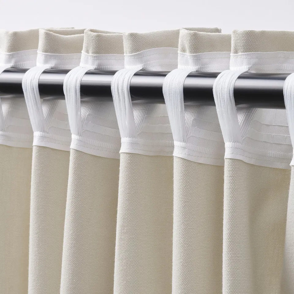 Close-up of beige curtains with metallic rod and white tabs for easy hanging.