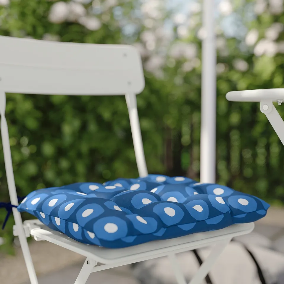 White metal balcony chair with blue, circular-patterned cushion. Outdoor setting.