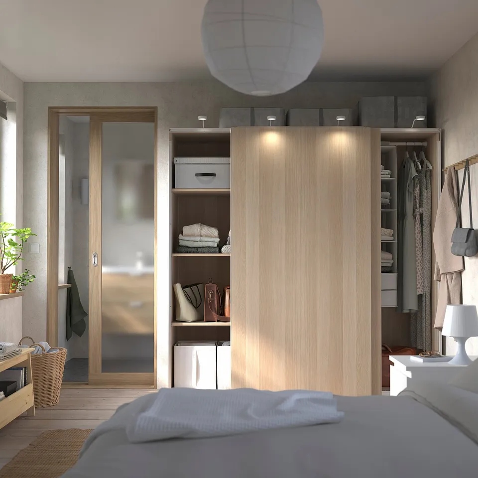 Modern bedroom with beige PAX wardrobe, mirrored doors, and white bed.