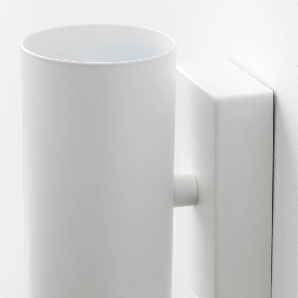 Modern white wall-mounted light fixture with rounded shade and sturdy base, emitting downward light.