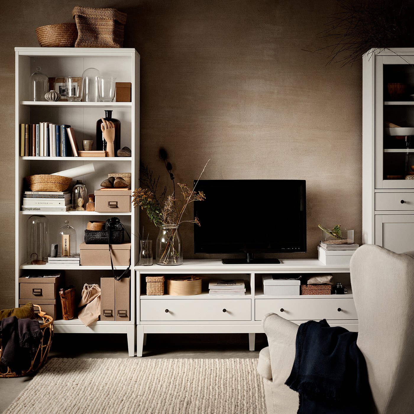 Living room with IDANÄS white shelves, tv, and beige armchairs.