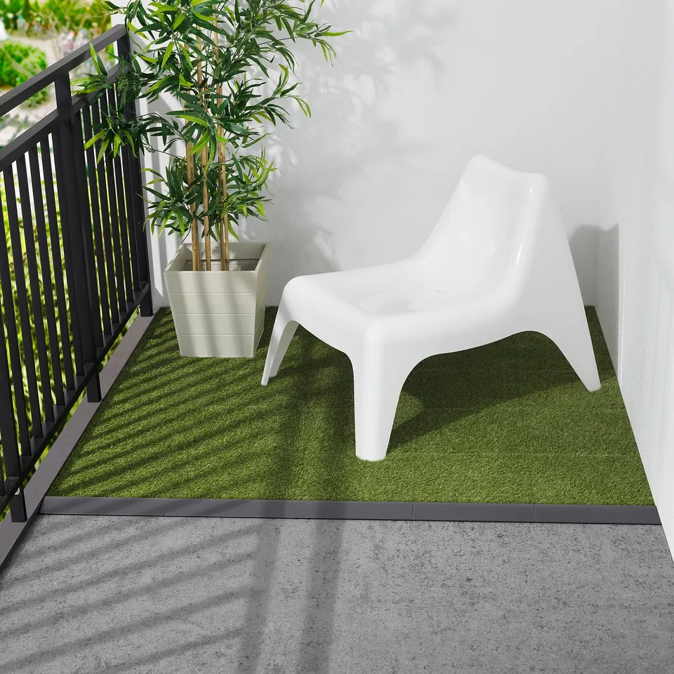 Modern mini balcony with white RUNNEN chair, small potted plant, dark railings, and artificial grass mat, creating a cosy green space.