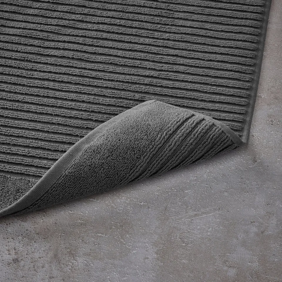 Dark grey bath mat and towel displayed on concrete floor, showcasing their textured, absorbent design.