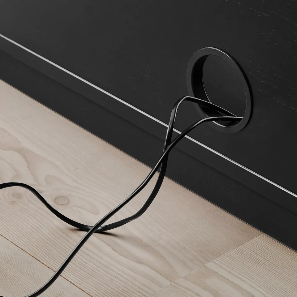 Black cable organiser on wooden floor. Cord outlet on unit for managing cords.
