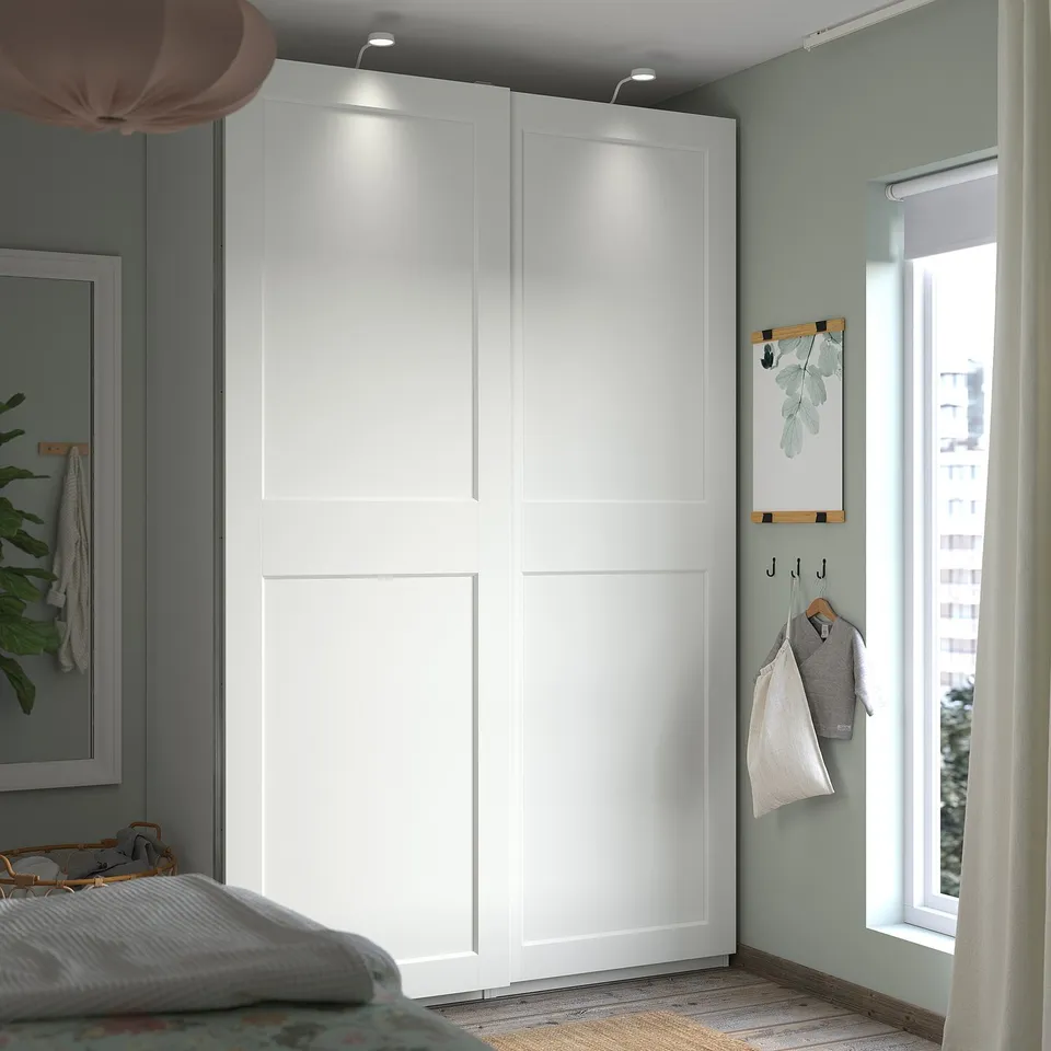 Modern bedroom with white PAX wardrobe, wooden hooks, grey walls, and natural light.