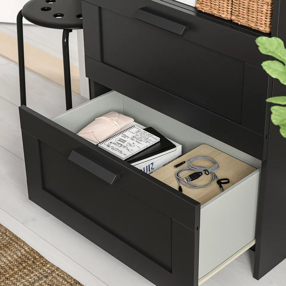 Black BRIMNES tv stand with open drawer showing folded blanket, books, and cables.