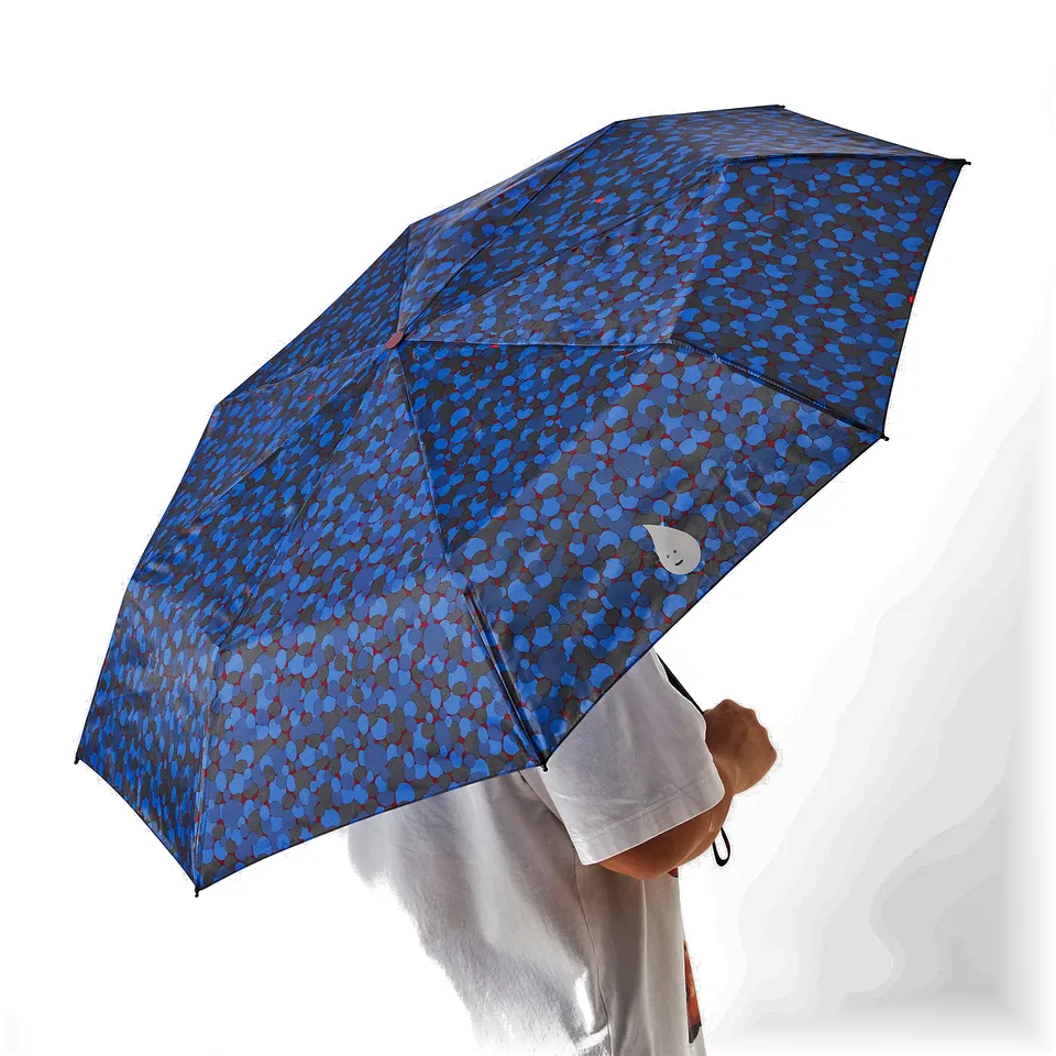 A person holding a blue patterned umbrella with large polka dots over their head.