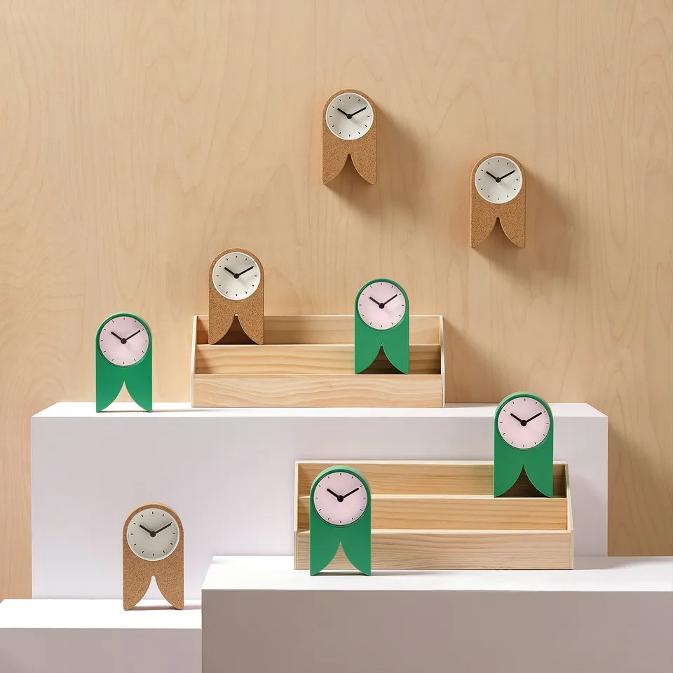 Aerial view of green & cork FLODKRÄFTA clocks on white walls with wooden background.