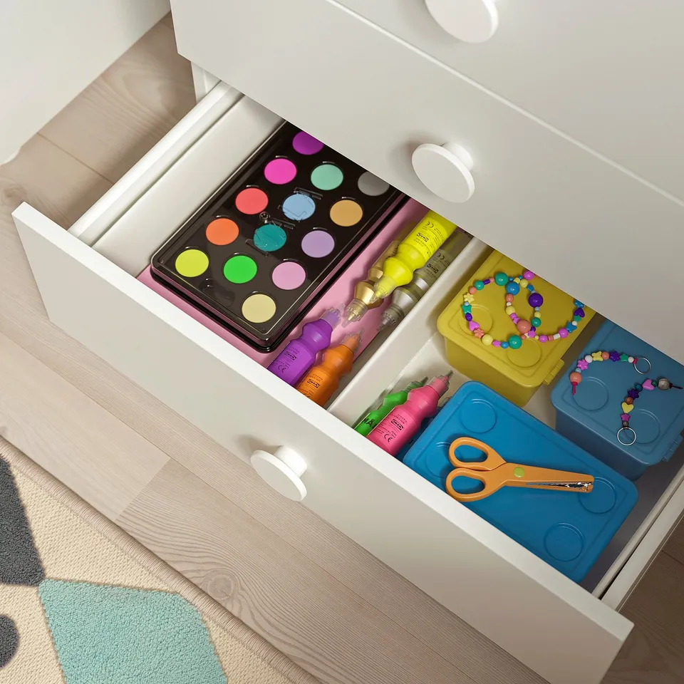 Open drawer reveals organised kids craft supplies: paints, markers, scissors, and beads in colourful containers.