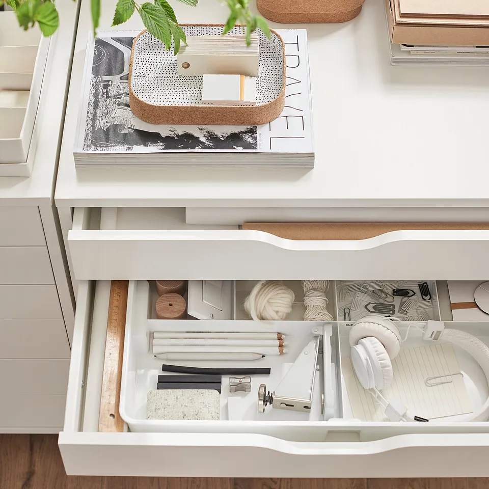 White ALEX drawers, organised with office supplies, books, and plants. Top drawer open, showing compartments.