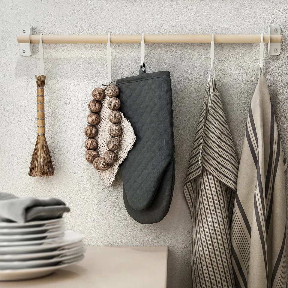 A kitchen scene with a wooden rod holding items like an oven mitt, striped towels, and a brush, indicating its a hanging storage solution.