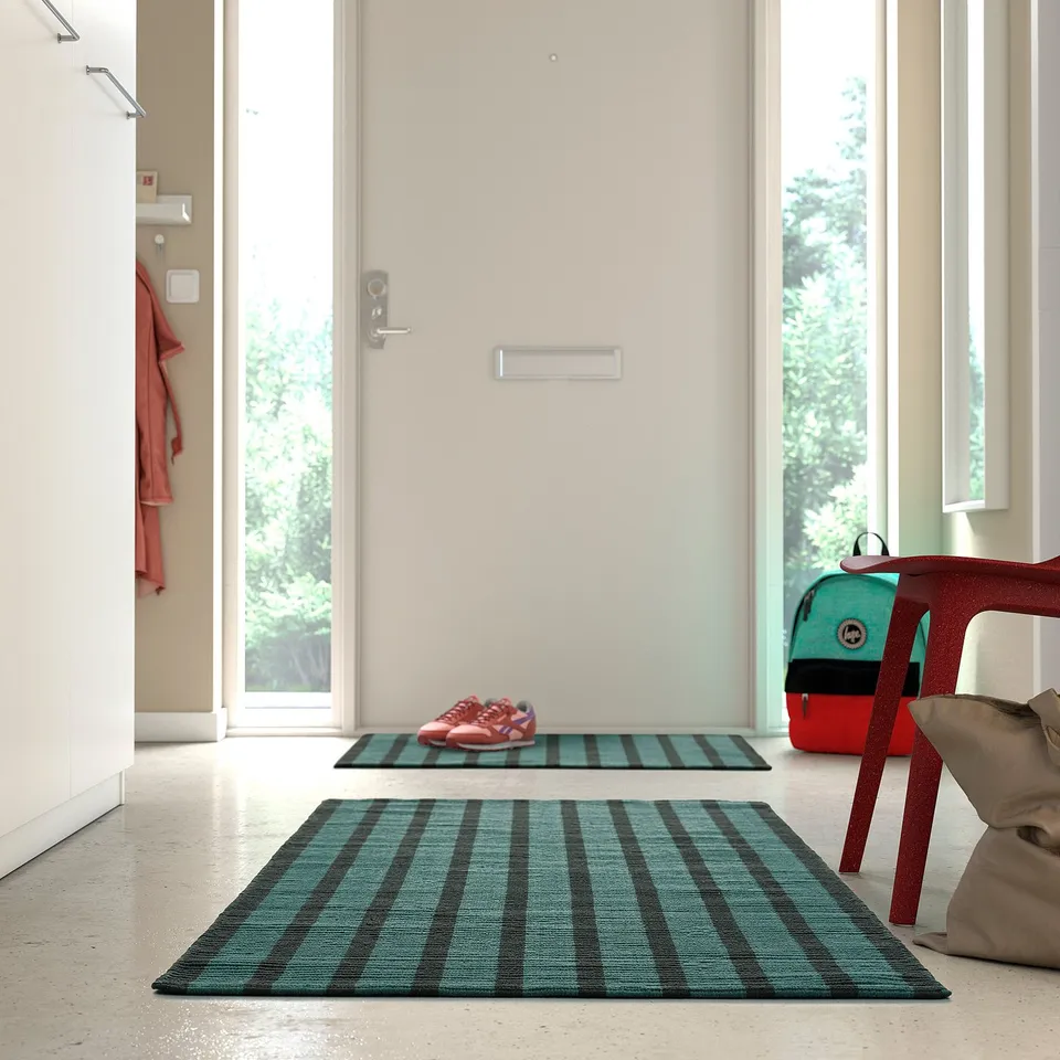 Blue-green striped VÄGSKYLT rug, rectangular, with matching mat and red chair.