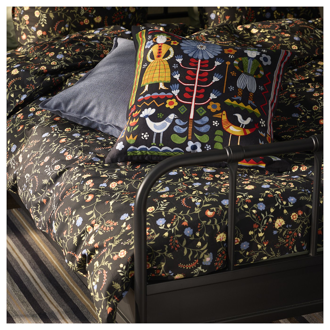 TRATTKAKTUS cushion on floral-patterned bed, featuring colourful swedish figures and nature.